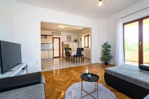 Ein modernes Wohnzimmer mit Flachbildfernseher, einer Couch, einem runden Couchtisch und einem Essbereich mit Tisch und Stühlen.