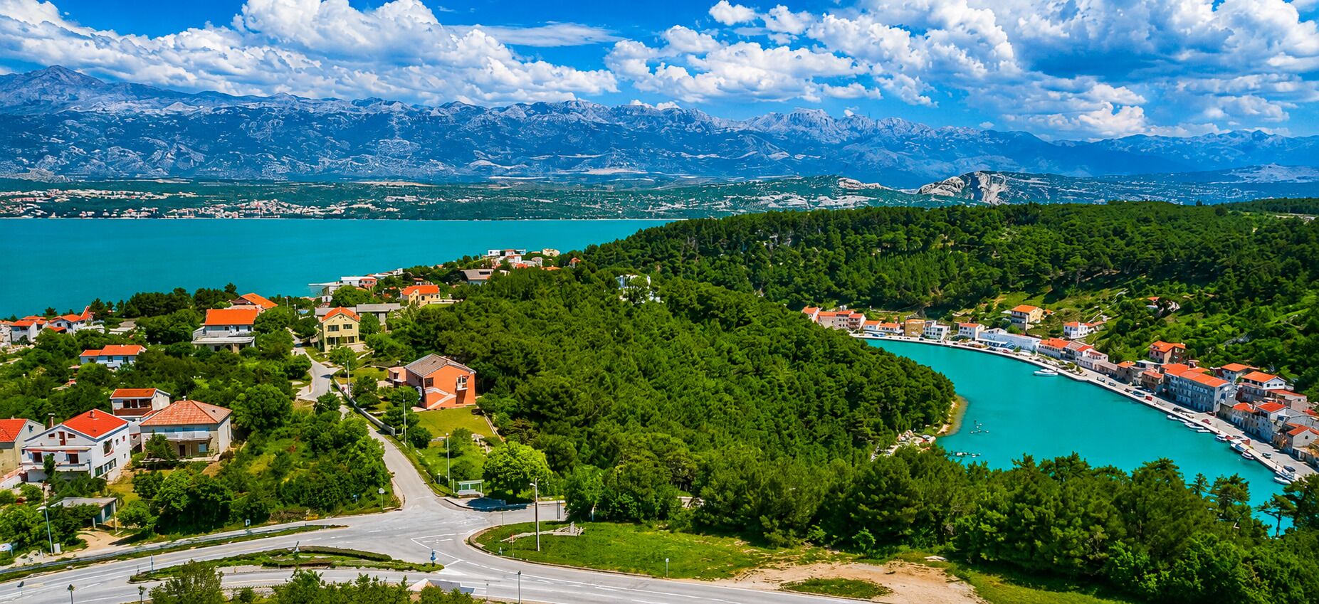 Une ville côtière dotée d’un port de plaisance, entourée de montagnes et d’une végétation luxuriante.