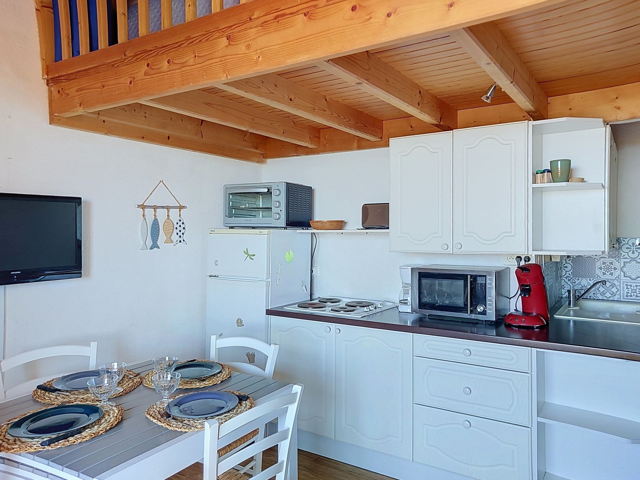 Una cocina compacta con armarios blancos, microondas, tostadora y cafetera.