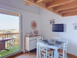 A dining area with a table set for four, a television mounted on the wall, and a view of the outside through a sliding door. - Les Terrasses de la Méditerranée by Interhome (Saint Pierre La Mer)