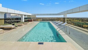 A rooftop infinity pool with a clear view of the cityscape, a depth marker, and lounge chairs. - Bloomfields Studio Condor Golf Links 18  (Dubai)