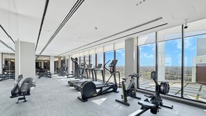 A modern gym with various exercise machines, large windows, and a high ceiling. - Bloomfields Studio Condor Golf Links 18  (Dubai)