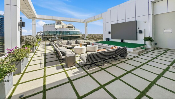A rooftop terrace with outdoor seating, a flat-screen TV, and a view of a modern building. - Bloomfields Studio Condor Golf Links 18  (Dubai)