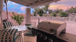 Un patio al aire libre con una parrilla, sillas y vistas al paisaje desértico.