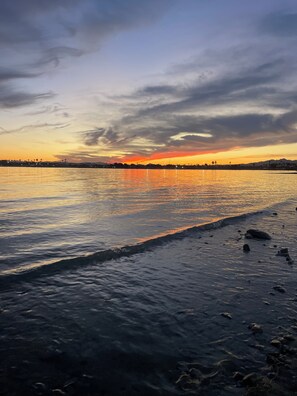 Ein Sonnenuntergang über ruhigem Wasser, im Hintergrund eine Küstenlinie.
