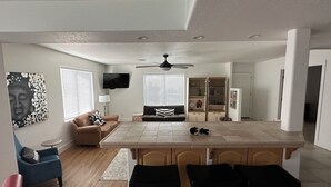 Una cocina moderna con una isla central, taburetes de bar, un sofá y un televisor.