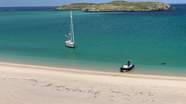 Una playa con un velero y un barco motorizado anclados cerca de la orilla.