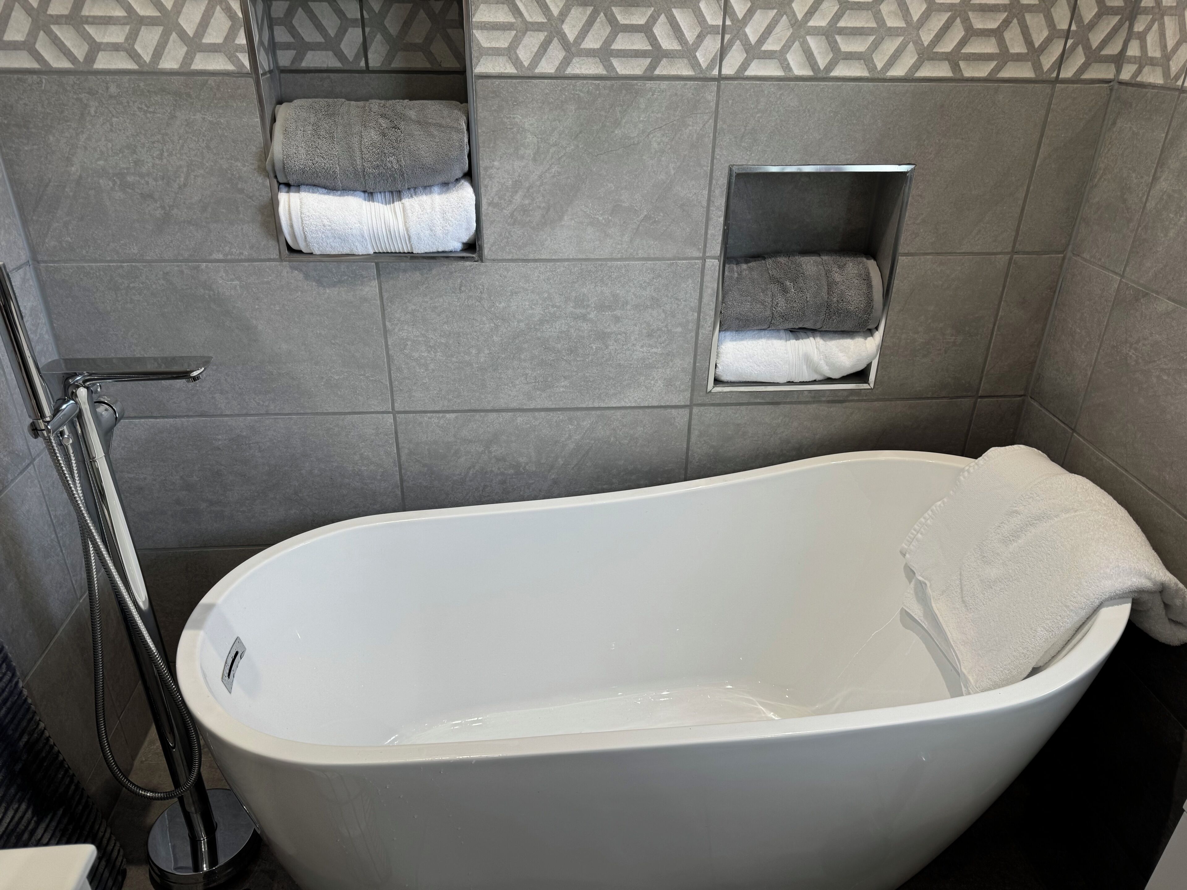 A modern bathroom with a freestanding bathtub, a showerhead, and two towel racks with towels.