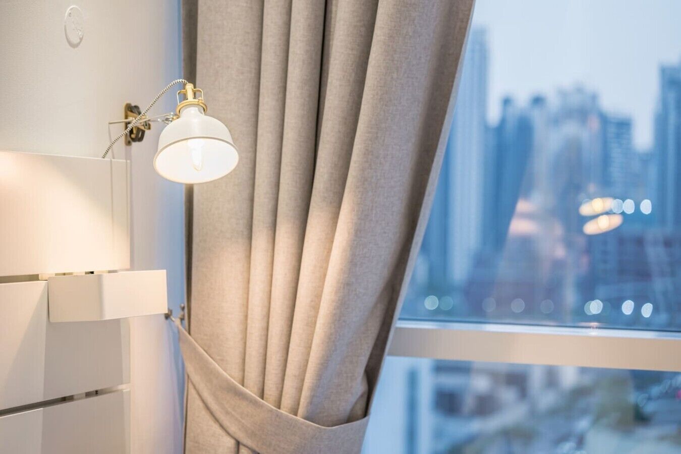 Een kamer met een raam, een gordijn en een wandlamp.