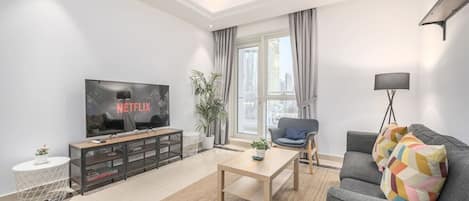 A modern living room with a flat-screen TV, a sofa, a coffee table, and a potted plant.