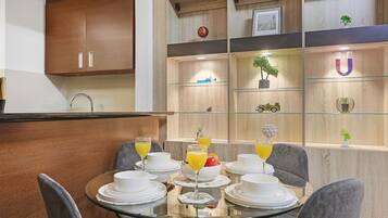 Un coin repas moderne avec une table en verre dressée pour le petit-déjeuner, des meubles en bois et des objets décoratifs disposés sur des étagères.