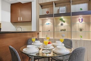 Een moderne eetruimte met een glazen tafel gedekt voor het ontbijt, houten kasten en decoratieve objecten op planken.