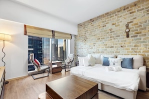 Een moderne hotelkamer met een groot bed, een bank, een bijzettafeltje en uitzicht op de skyline door grote ramen.