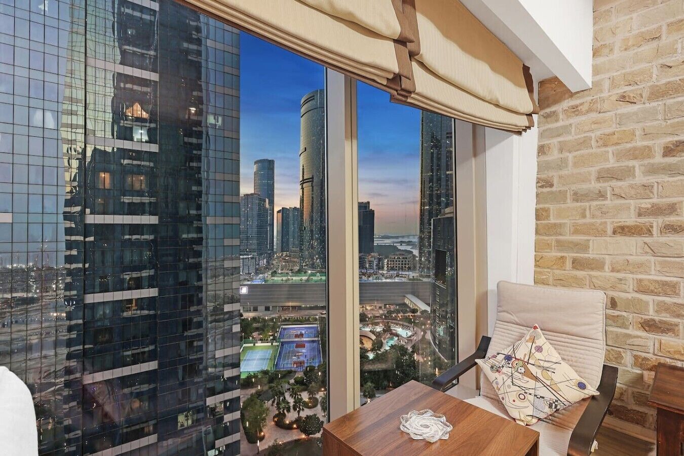 Un balcon avec vue sur la ville, une chaise rembourrée, une petite table et un mur en briques.
