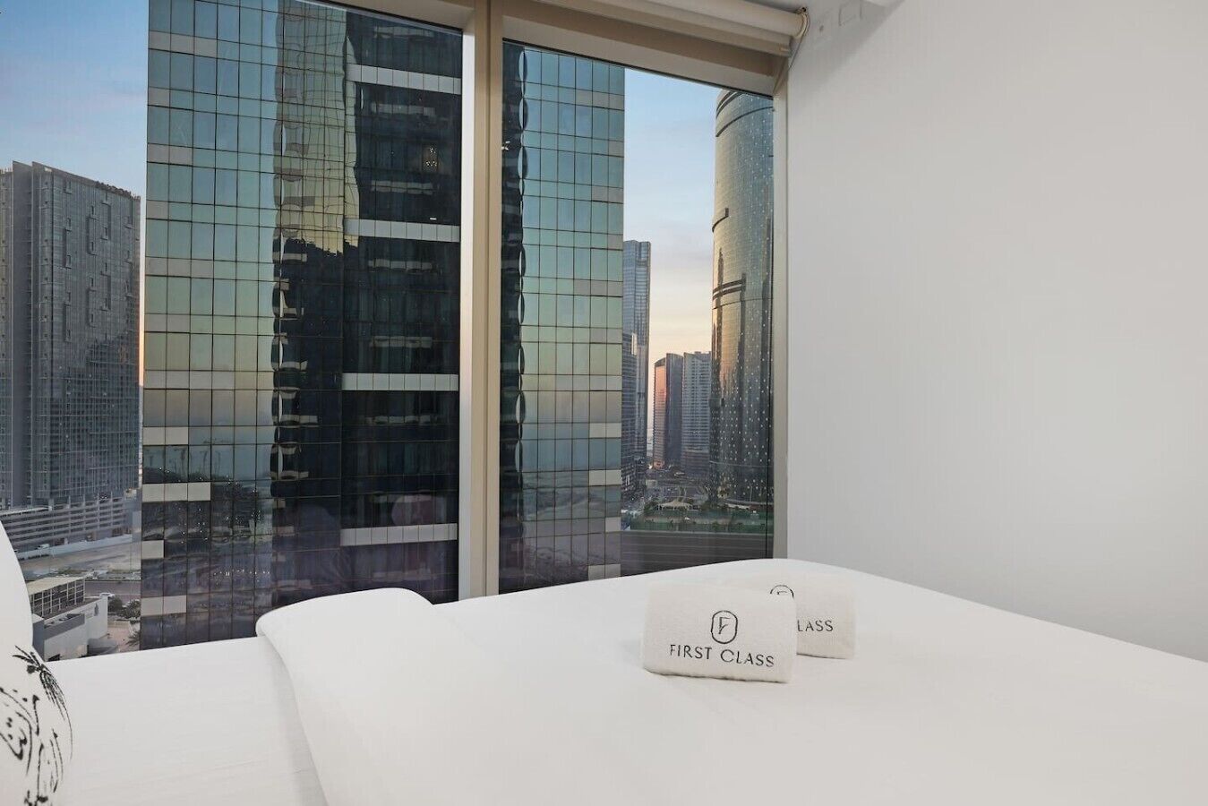A modern hotel room with a large window, a bed, and a view of tall buildings.
