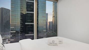 A modern hotel room with a large window, a bed, and a view of tall buildings.