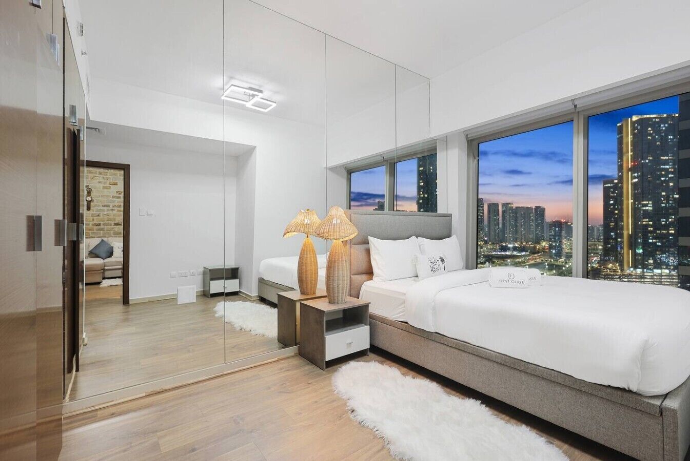 Une chambre moderne avec vue sur la ville, un grand lit, des tables de chevet et un miroir.
