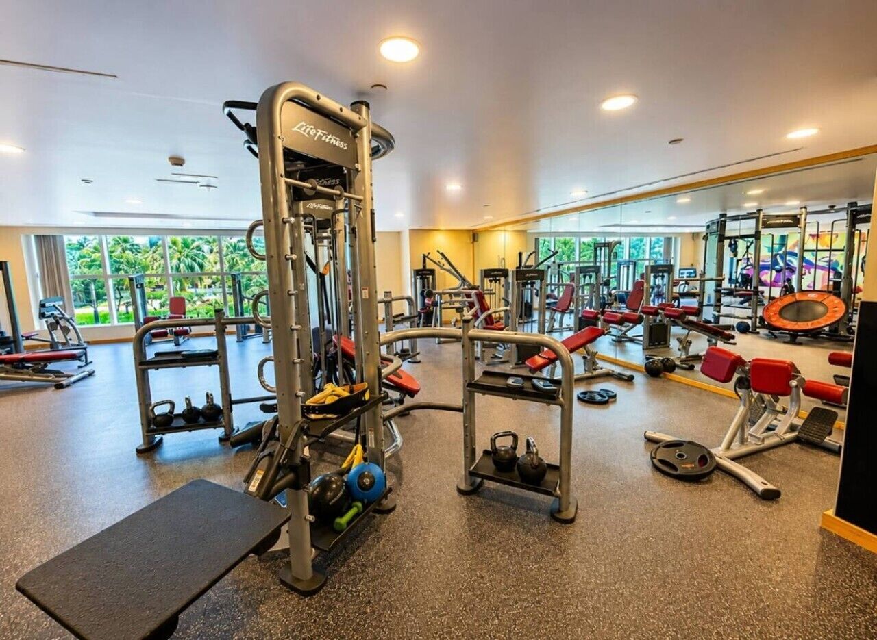 A gym with various exercise equipment, a bench, and a mirrored wall.