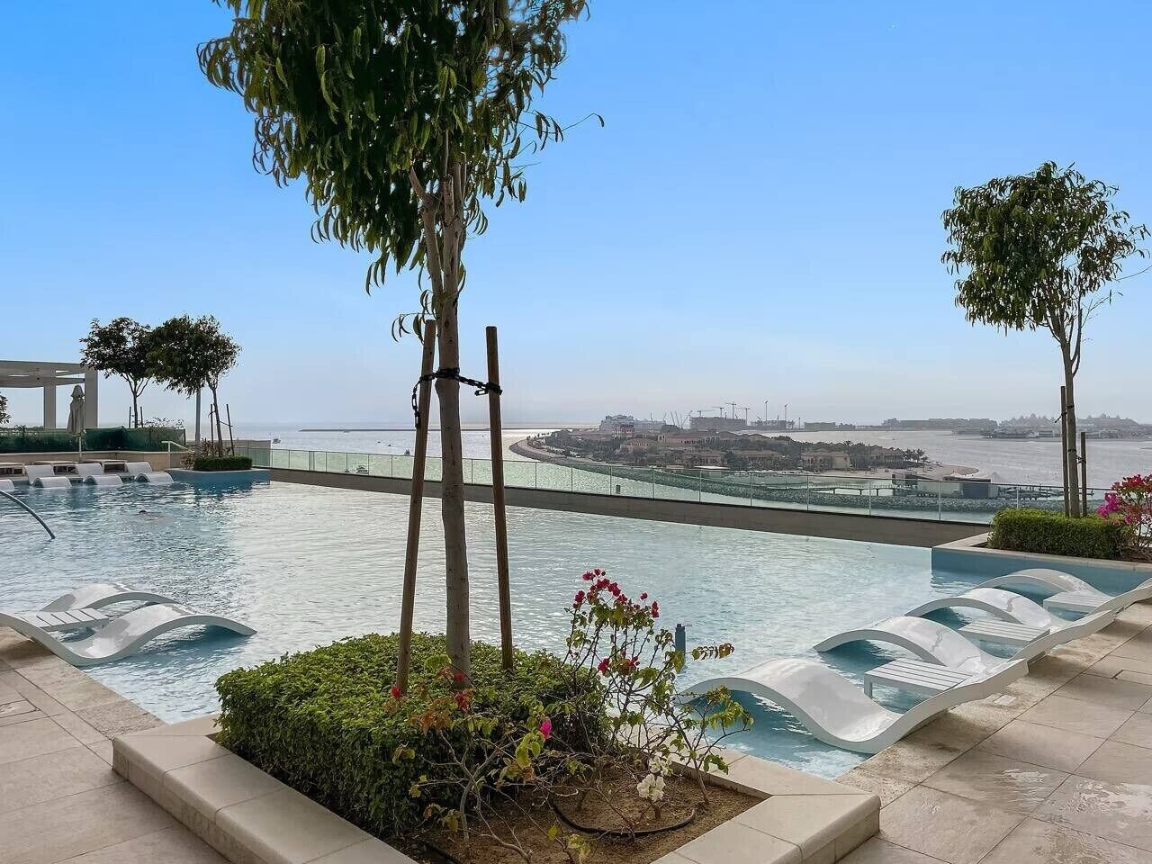 Une piscine avec vue sur la mer et un pont, entourée de verdure et bordée d’une architecture moderne.