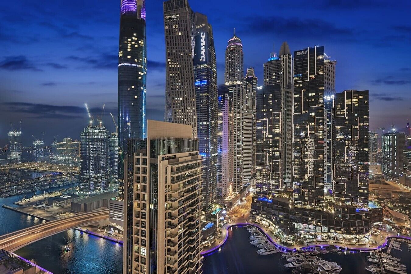 A cityscape with high-rise buildings, a marina, and a bridge.