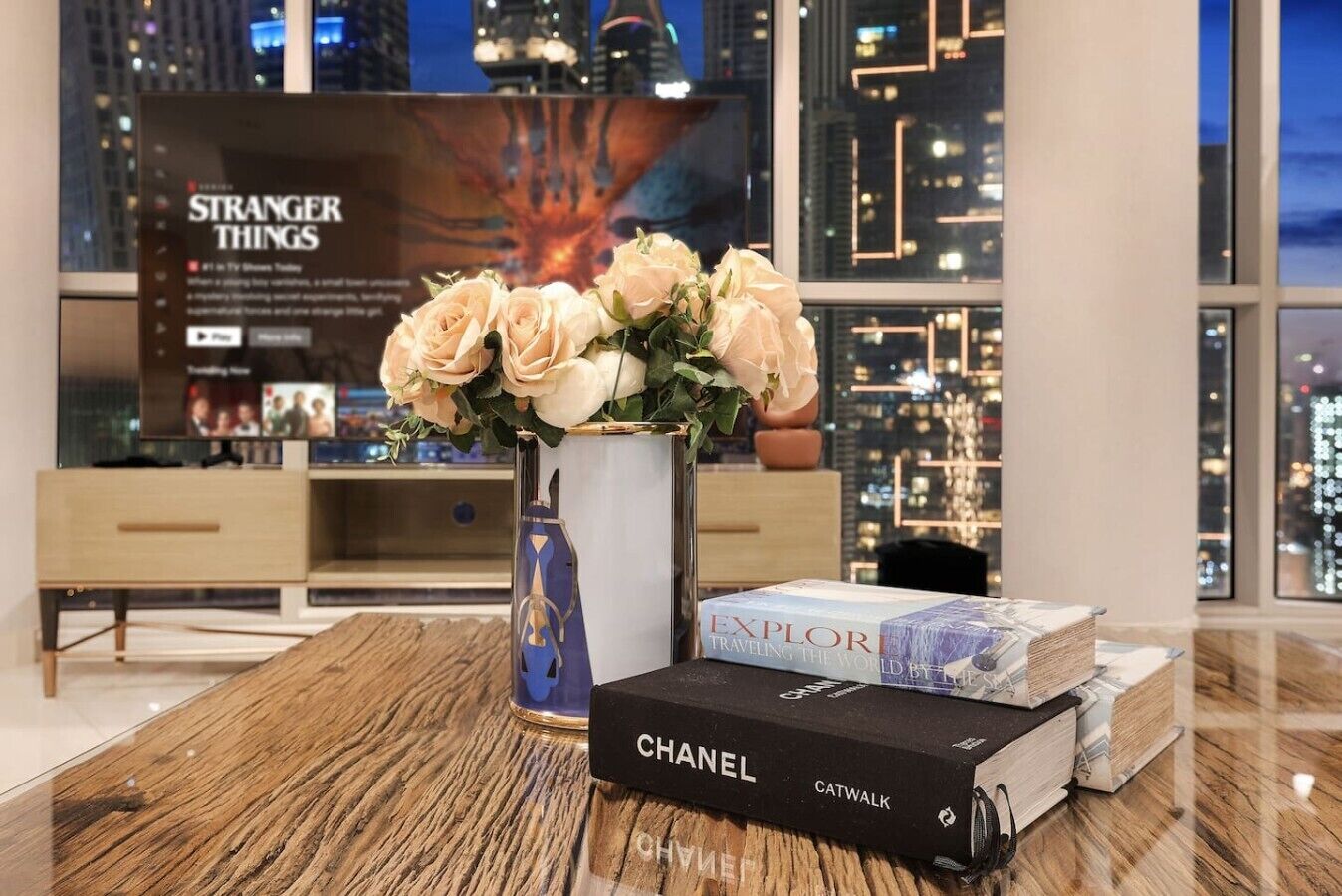 Ein modernes Interieur mit einem Holztisch, einer Blumenvase, einem Buch von Chanel und einem 'Stranger Things' Poster.