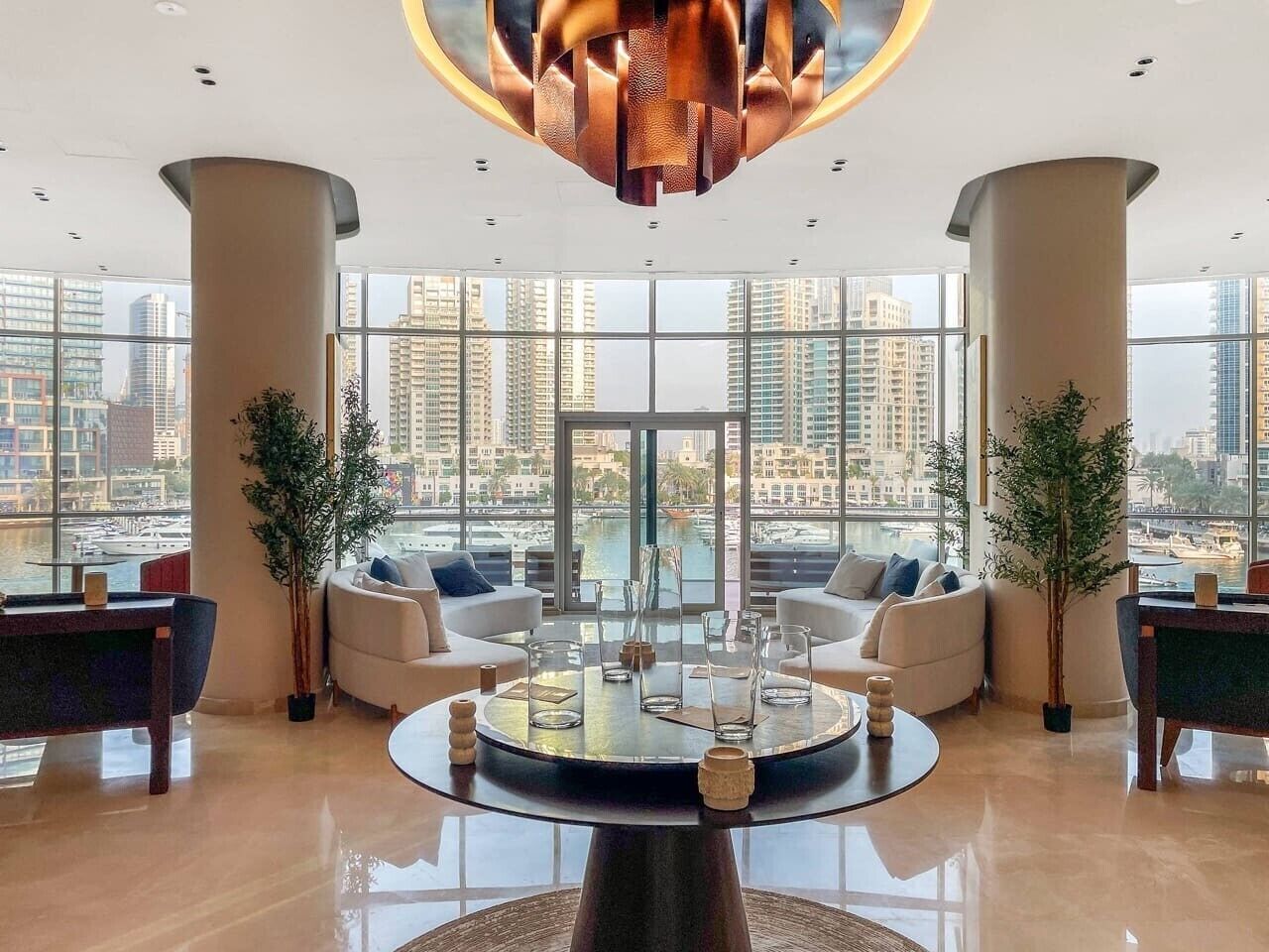 A spacious lobby with a central coffee table, seating area, and large windows offering a city view.