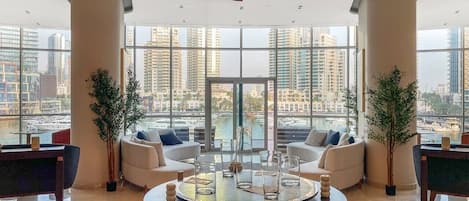 A spacious lobby with a central coffee table, seating area, and large windows offering a city view.