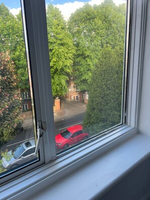 A window with a view of a street, trees, and a building. - Stylish Renovated 2BR Apartment in South London (London)