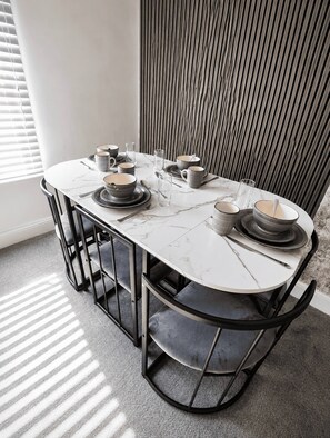 A dining table set with plates, bowls, and glasses, surrounded by chairs with a modern design. - Stylish Renovated 2BR Apartment in South London (London)