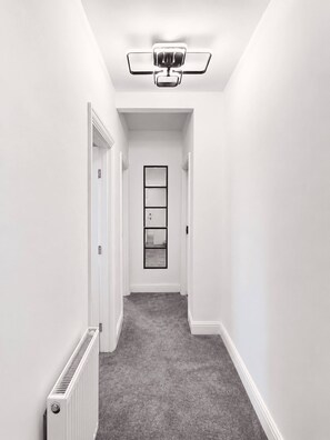 A narrow hallway with a radiator on the left, a ceiling fan, and a door at the end. - Stylish Renovated 2BR Apartment in South London (London)