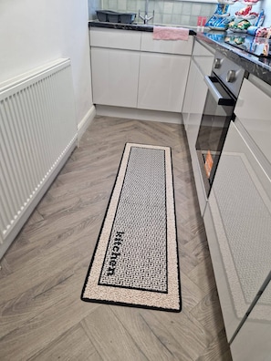 Eine Küche mit weißen Schränken, einer schwarzen Arbeitsplatte und einer Fußmatte mit Muster.