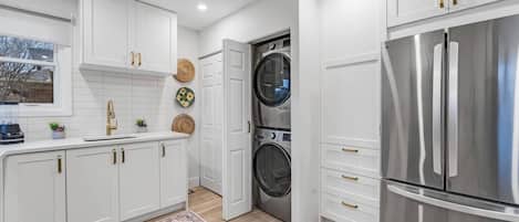 Una cocina moderna con armarios blancos, un refrigerador de acero inoxidable y una lavadora.
