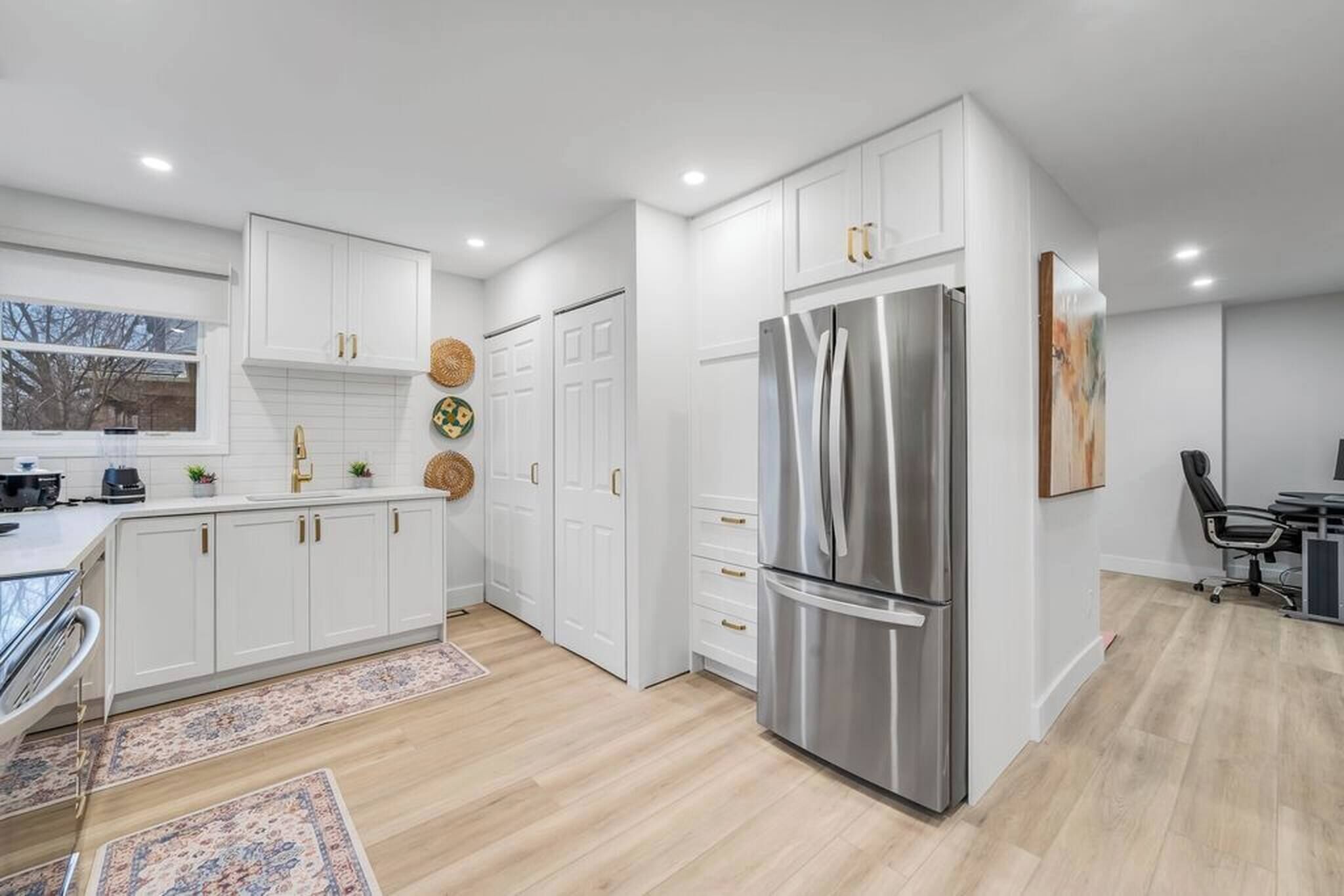 A modern kitchen with white cabinetry, a stainless steel refrigerator, and a dining area with a table and chairs.