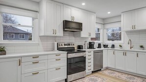 A modern kitchen with white cabinetry, stainless steel appliances, and a window providing a view of the outside. - Downtown luxury house close to the nature (Ottawa)