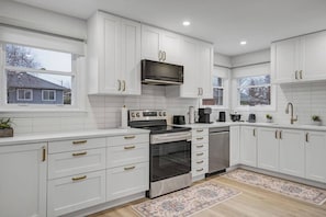 A modern kitchen with white cabinetry, stainless steel appliances, and a window providing a view of the outside. - Downtown luxury house close to the nature (Ottawa)