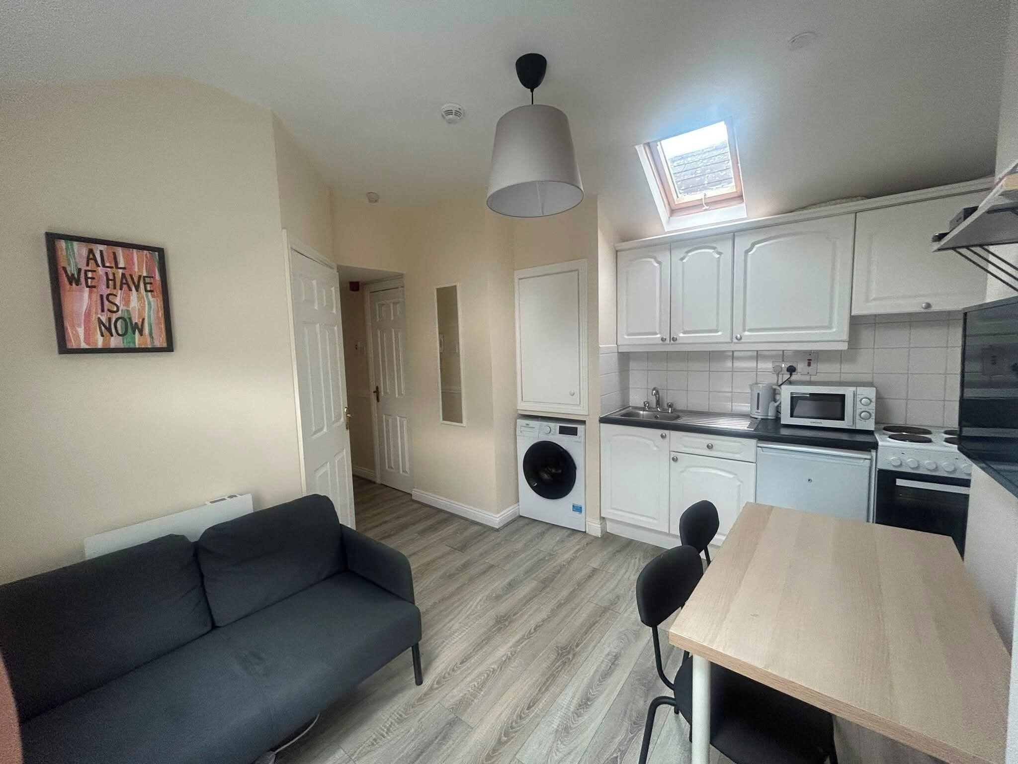 A compact kitchen with a washing machine, a dining table, and a sofa.