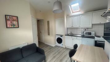 A compact kitchen with a washing machine, a dining table, and a sofa.