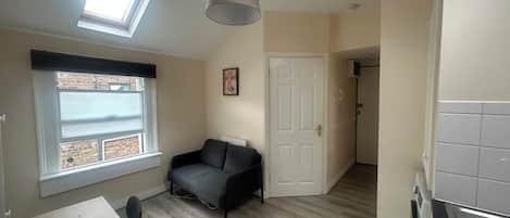 A compact living space with a kitchenette, a dining area, a sofa, and a window with a view.