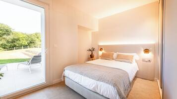 Een slaapkamer met een groot bed, een nachtkastje met een lamp en uitzicht op een tuin via een schuifdeur.