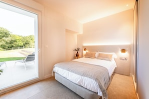 Un dormitorio con una cama grande, una mesita de noche con lámpara y vistas a un jardín a través de una puerta corredera.