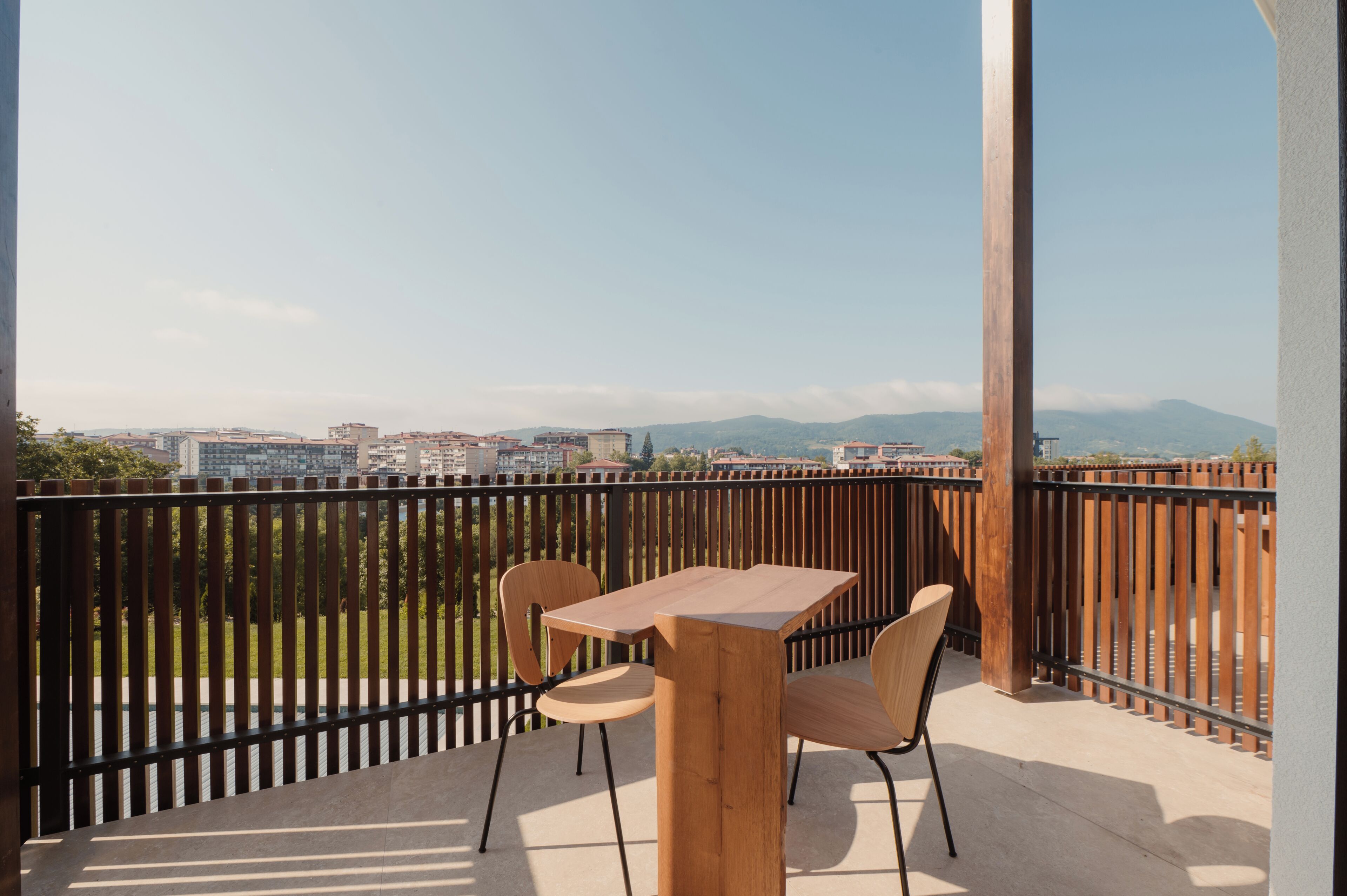 Un balcón con mesa y sillas, que ofrece vistas a la ciudad y a las montañas.