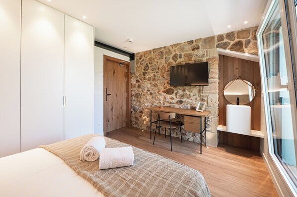 A bedroom with a bed, a desk, a chair, a TV, and a stone wall.