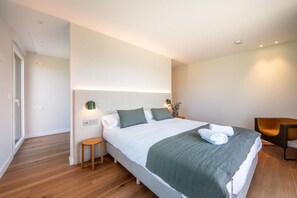 A modern hotel room with a large bed, bedside tables, a chair, and a view of the hallway.