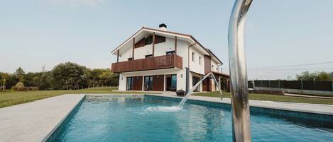A modern two-story house with a swimming pool in the foreground.