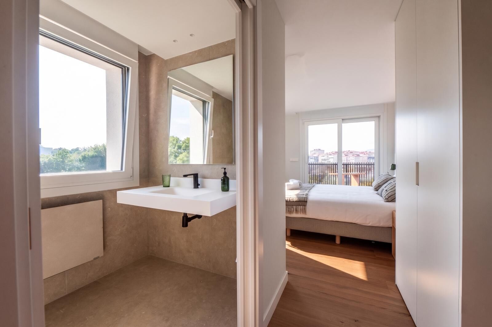Ein modernes Schlafzimmer mit einem großen Bett, einem Fenster und einem Badezimmer mit Waschbecken und Spiegel.