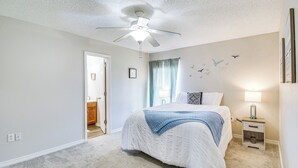 Une chambre à coucher comprenant un lit, un ventilateur de plafond, une table de chevet, une lampe et un mur décoré d’autocollants représentant des oiseaux.