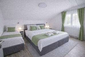 Ein Hotelzimmer mit einem großen Bett, zwei Nachttischen mit Lampen, einem Fenster mit grünen Vorhängen und Blick ins Grüne.