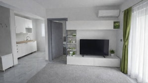 A modern living room with a flat-screen TV, built-in shelves, a kitchen area, and a door leading to another room. - Plitvice Green apartment with Sauna for families 1-8 people (Smoljanac)
