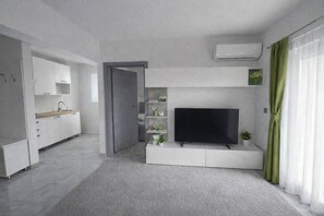 Ein modernes Wohnzimmer mit Flachbildfernseher, eingebauten Regalen, einer Küchenzeile und einer Tür zu einem weiteren Raum.