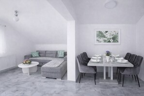 A modern living room with a grey sofa, a white coffee table, and a dining area with a grey table and chairs. - Plitvice Green apartment with Sauna for families 1-8 people (Smoljanac)